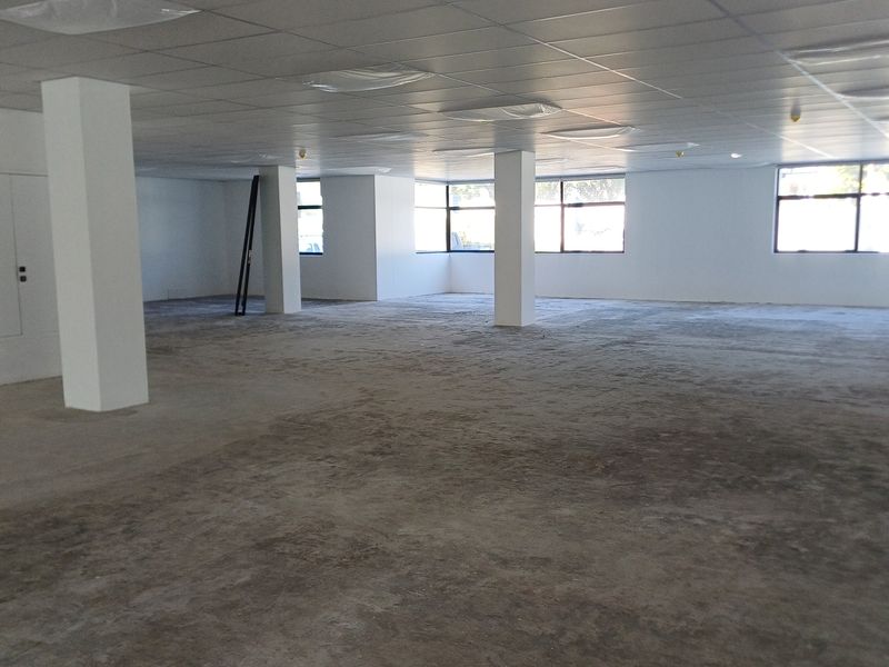 A large, open-plan office space featuring a suspended ceiling, structural columns, and expansive windows, currently awaiting final flooring installation.