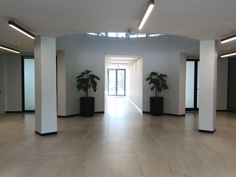 A spacious and modern office building entrance lobby featuring tiled flooring, structural columns, and bright recessed ceiling lighting.