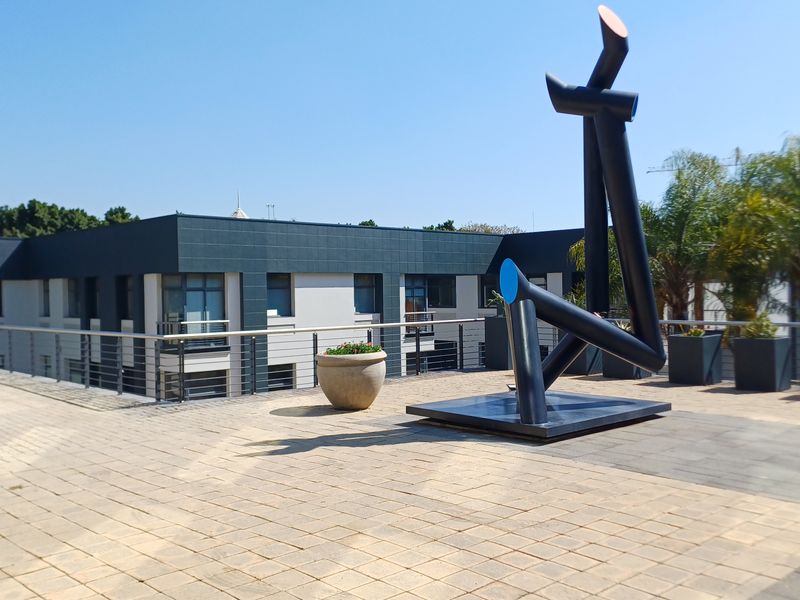 Spacious outdoor terrace featuring paved flooring, modern stainless steel railings, and views of the office building facade.