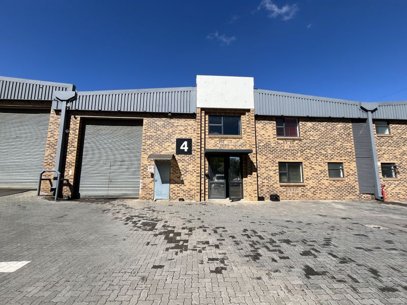 Front elevation of an industrial unit featuring a roller shutter door, brick facade, and paved driveway access.