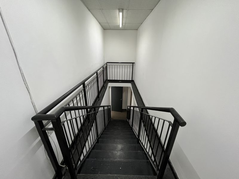 A functional industrial staircase featuring a metal balustrade and a suspended ceiling with integrated lighting, providing access between levels.