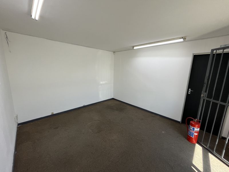 An empty industrial office space featuring fluorescent lighting, a security gate, and carpeted flooring, suitable for a variety of business uses.