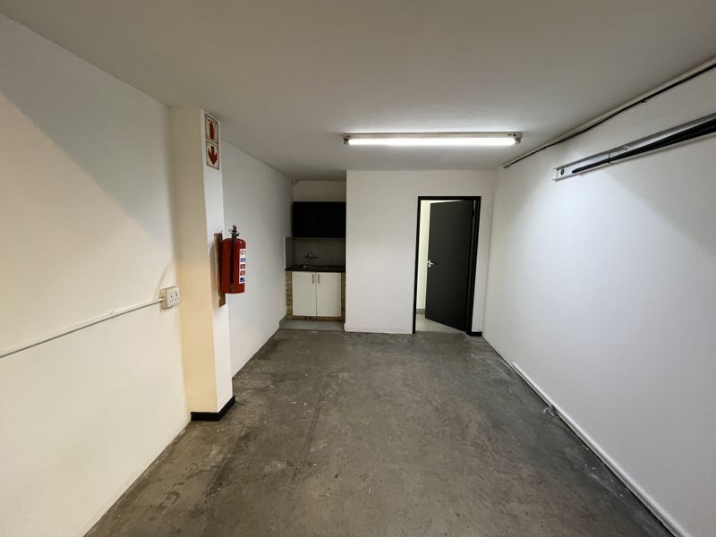 A clean, functional utility space featuring concrete flooring, a small built-in kitchenette, and a wall-mounted fire extinguisher.