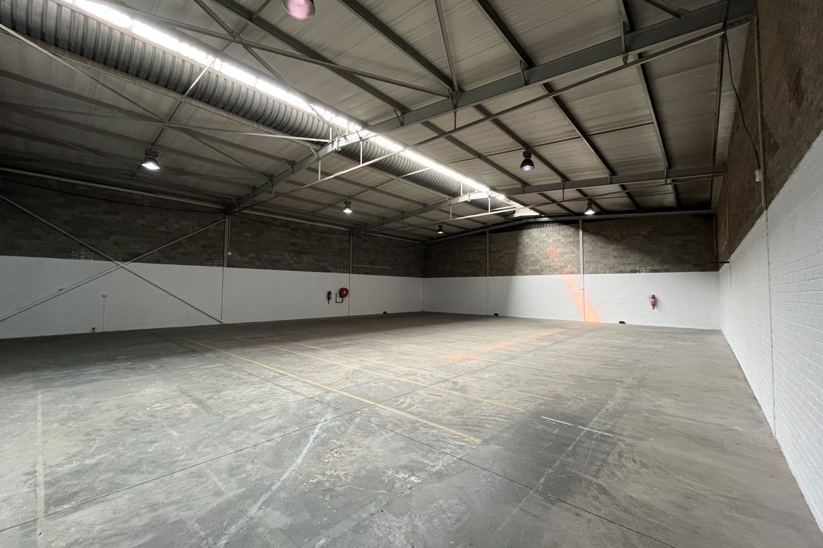 Spacious industrial warehouse unit featuring high ceilings with exposed steel trusses, concrete flooring, and functional industrial lighting throughout.