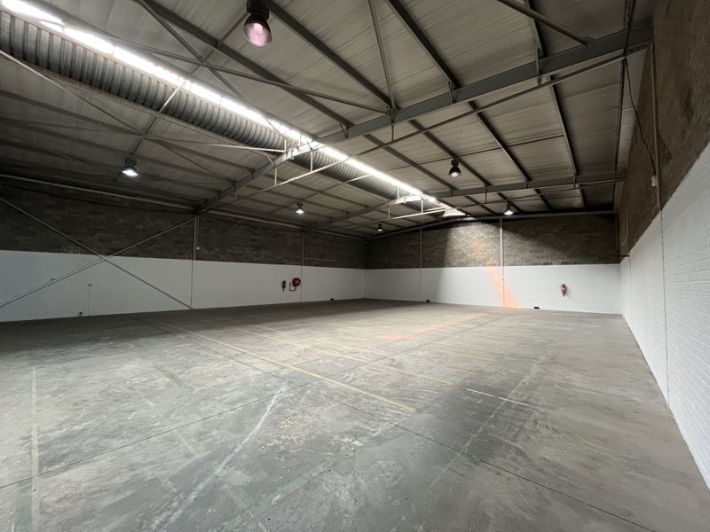 Spacious industrial warehouse unit featuring high ceilings with exposed steel trusses, concrete flooring, and functional industrial lighting throughout.