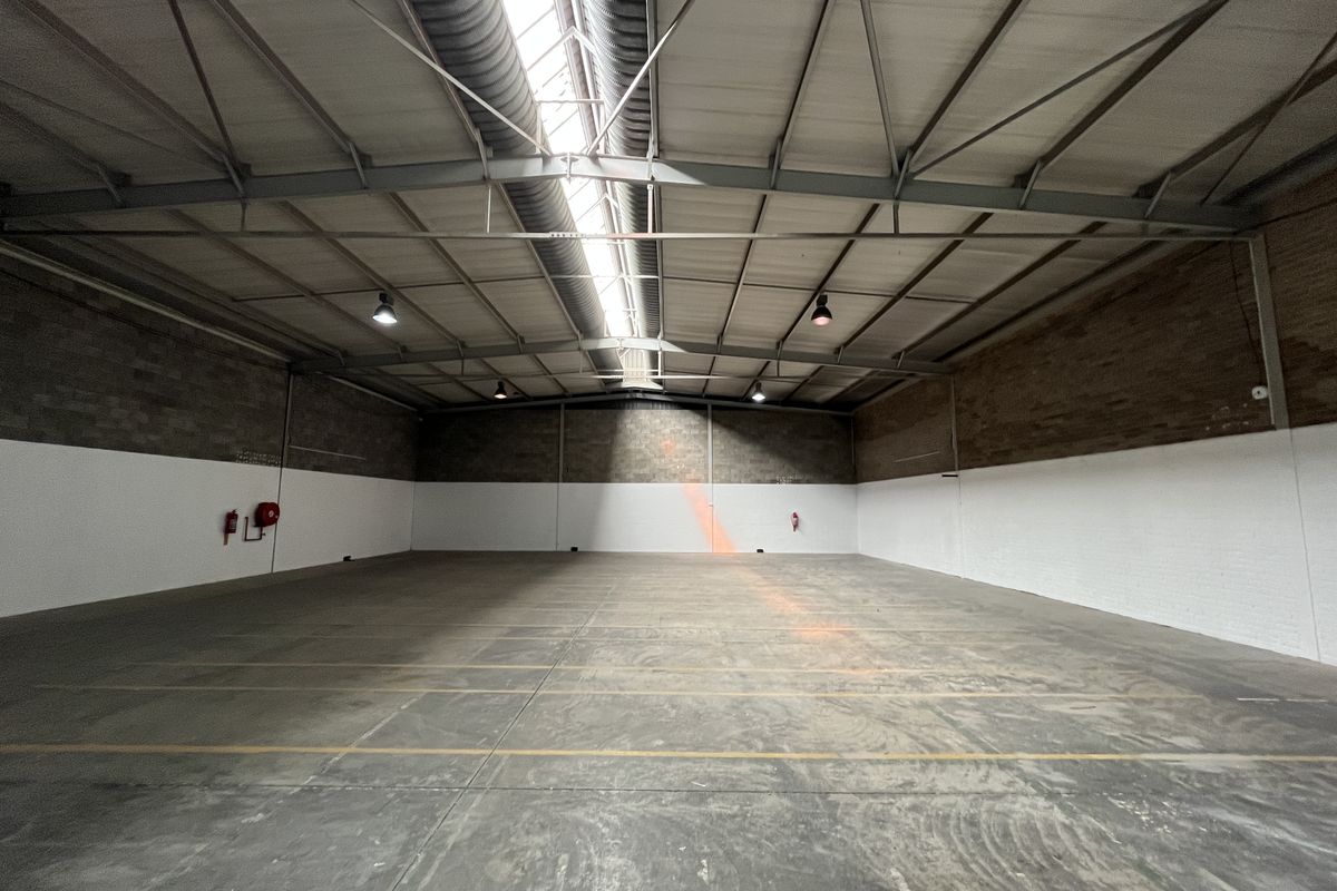Spacious industrial warehouse unit featuring high ceilings with exposed steel trusses, skylights, concrete flooring, and functional industrial lighting.