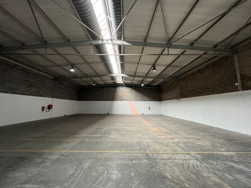 Spacious industrial warehouse unit featuring high ceilings with exposed steel trusses, skylights, concrete flooring, and functional industrial lighting.