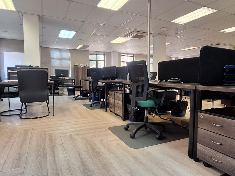 A spacious open-plan office area featuring modern herringbone flooring, suspended ceilings with recessed lighting, and structural support columns.
