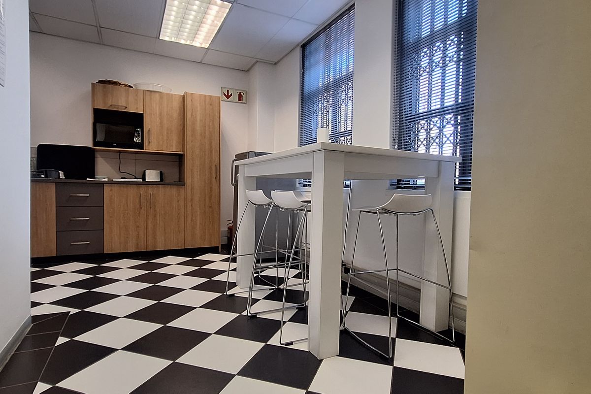 A functional office kitchenette featuring built-in cabinetry, laminate countertops, and distinctive checkered floor tiles, providing a practical break area for staff.