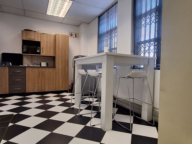 A functional office kitchenette featuring built-in cabinetry, laminate countertops, and distinctive checkered floor tiles, providing a practical break area for staff.