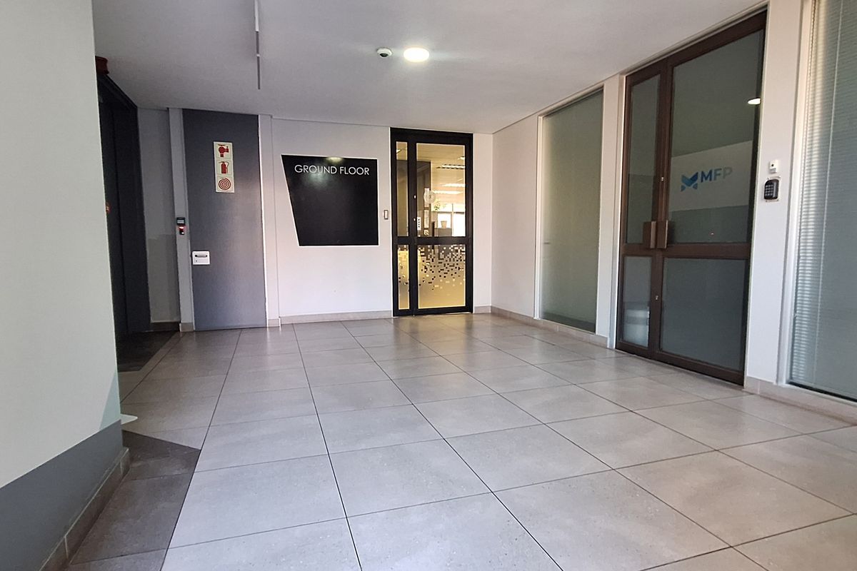 A clean and professional ground floor office building entrance featuring tiled flooring, glass partition doors, and modern access control systems.