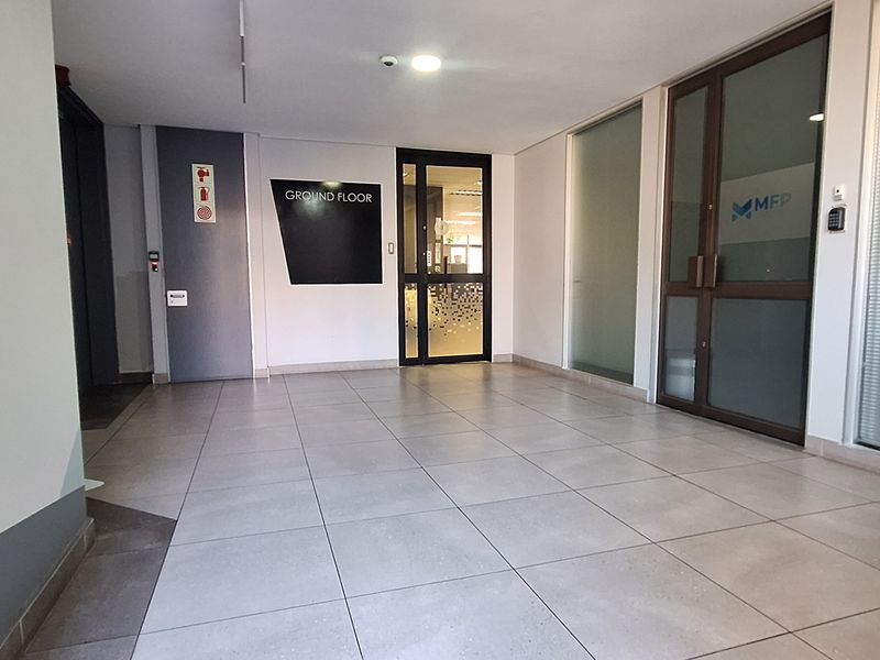 A clean and professional ground floor office building entrance featuring tiled flooring, glass partition doors, and modern access control systems.