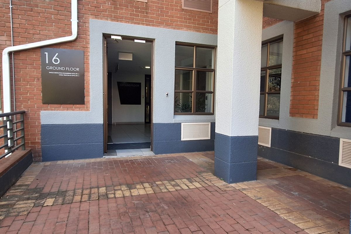 Ground floor office entrance featuring a brick facade, paved walkway, and professional signage, providing clear access to the building interior.