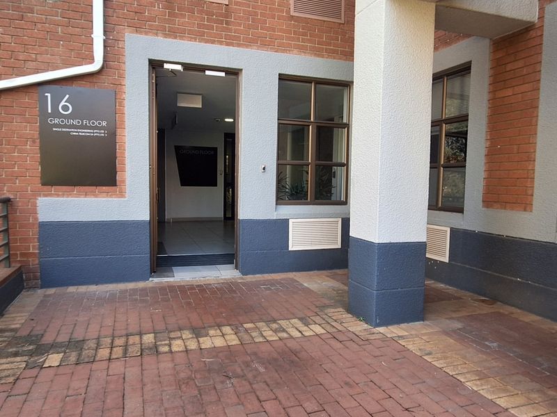 Ground floor office entrance featuring a brick facade, paved walkway, and professional signage, providing clear access to the building interior.