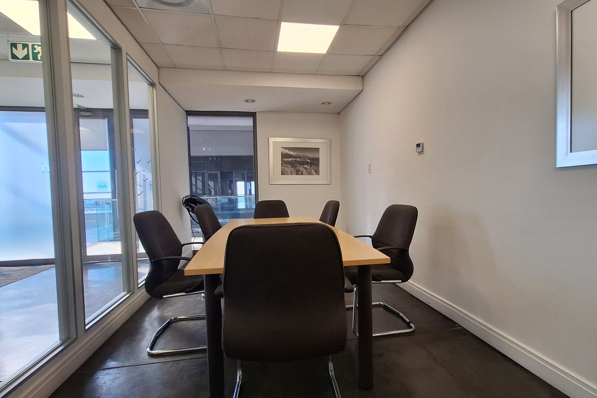 A professional office meeting room featuring a glass partition wall, suspended ceiling with recessed lighting, and tiled flooring.