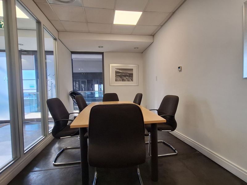 A professional office meeting room featuring a glass partition wall, suspended ceiling with recessed lighting, and tiled flooring.