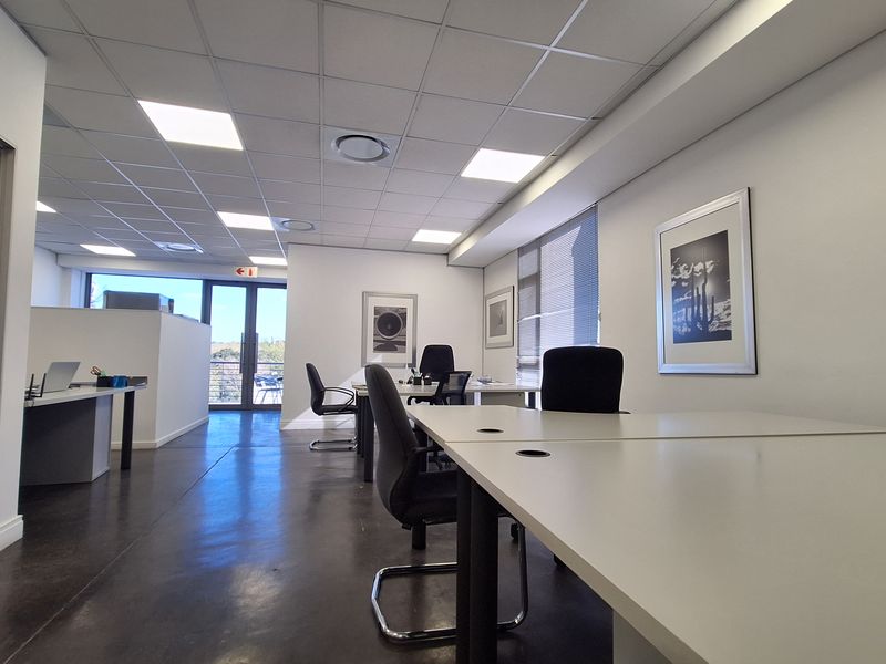 Modern open-plan office space featuring polished concrete floors, suspended ceiling with recessed LED lighting, and access to an outdoor area via glass doors.