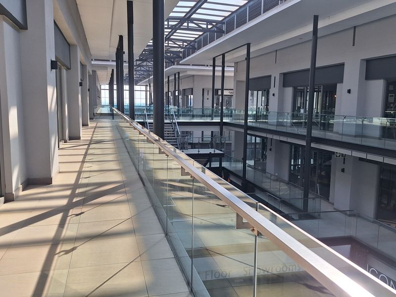 A modern, multi-level office atrium featuring a glass balustrade, tiled walkways, and an expansive skylight roof structure providing natural light.
