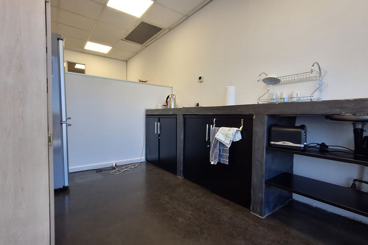 A functional office kitchenette featuring a concrete countertop, black cabinetry, and a stainless steel sink, set within a clean, professional workspace.