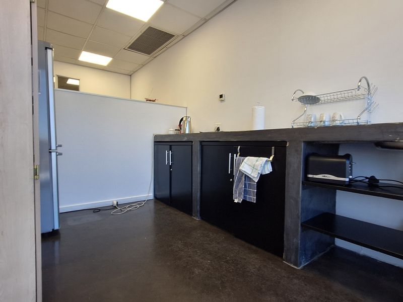 A functional office kitchenette featuring a concrete countertop, black cabinetry, and a stainless steel sink, set within a clean, professional workspace.