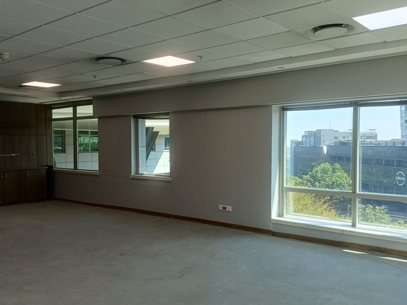 A spacious, empty office area featuring built-in cabinetry, large windows with city views, and a suspended ceiling with recessed lighting.
