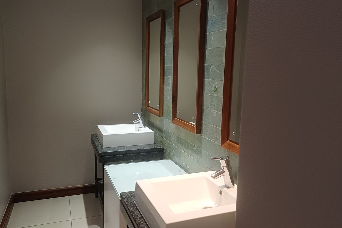 A modern office bathroom featuring dual vessel sinks, granite countertops, and a stylish stone tile backsplash with matching framed mirrors.