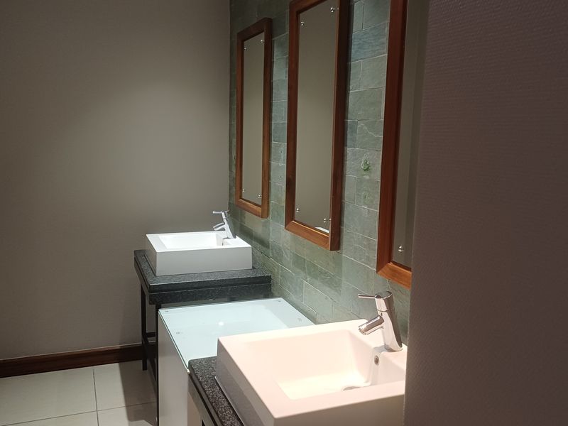 A modern office bathroom featuring dual vessel sinks, granite countertops, and a stylish stone tile backsplash with matching framed mirrors.