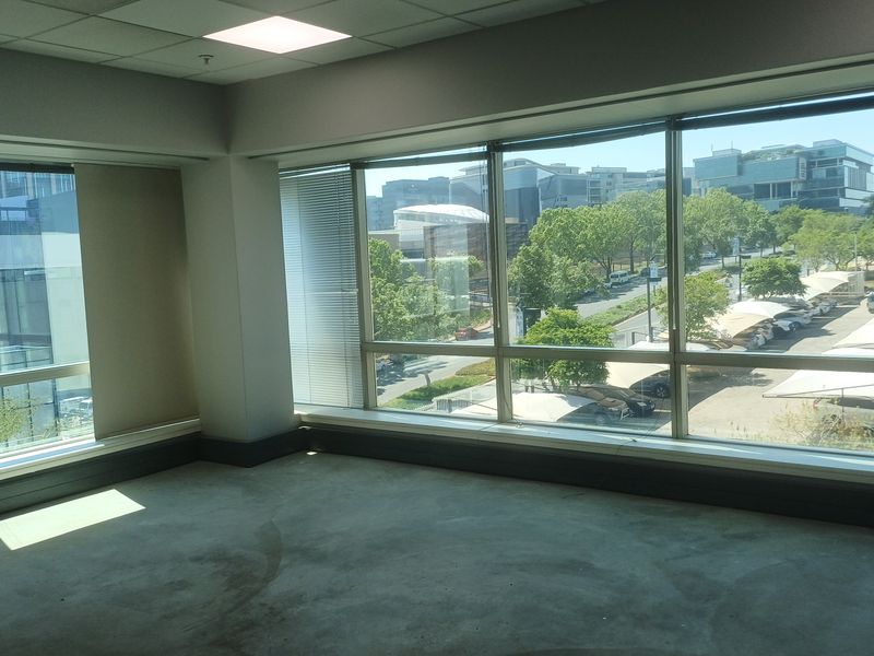 An empty, open-plan office space featuring large windows with natural light, suspended ceilings, and views of the surrounding business park.