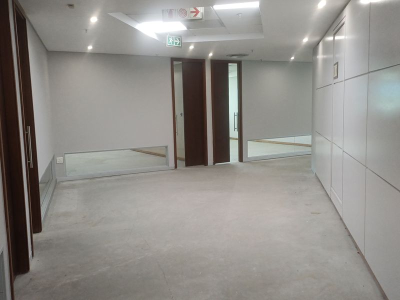 A spacious, empty office hallway featuring modern modular wall paneling, recessed lighting, and timber doors, currently awaiting final floor finishes.