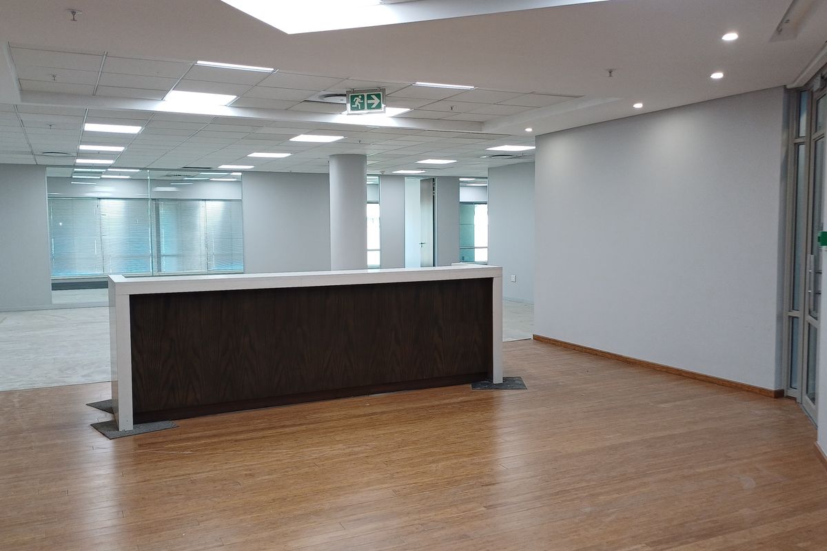 Spacious open-plan office area featuring a built-in reception desk, modern suspended ceiling with recessed lighting, and durable laminate flooring.