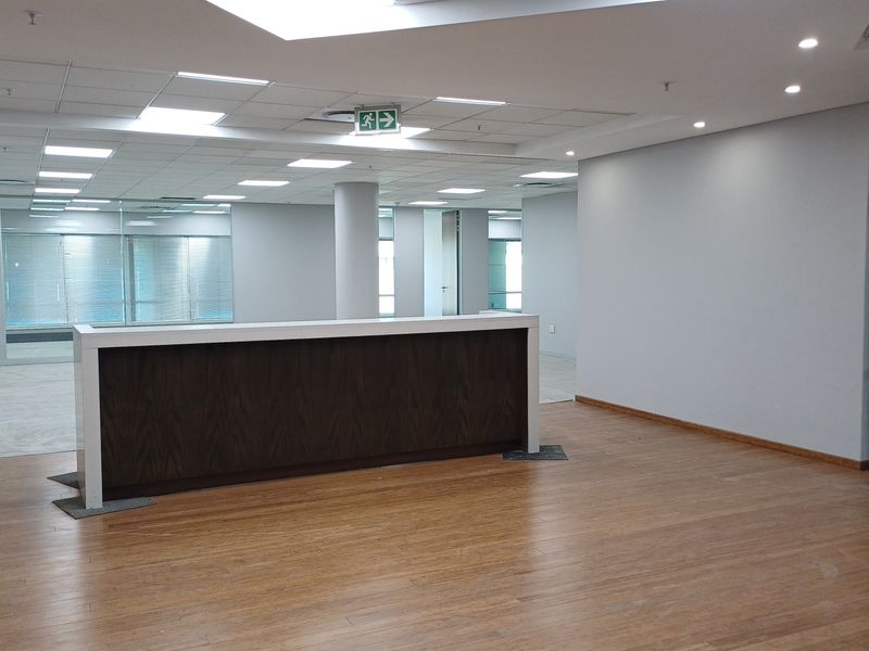 Spacious open-plan office area featuring a built-in reception desk, modern suspended ceiling with recessed lighting, and durable laminate flooring.
