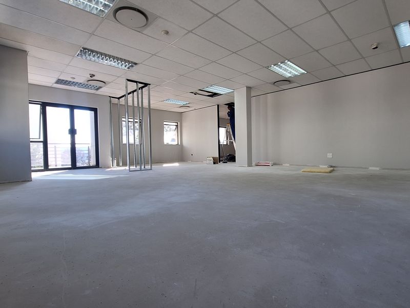 Open-plan office space currently undergoing renovations, featuring a suspended ceiling, recessed lighting, and large windows with access to an exterior balcony.