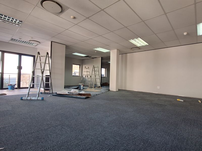 Spacious open-plan office area featuring suspended ceilings, recessed lighting, and carpet tiles, currently undergoing minor finishing works with direct access to a balcony.