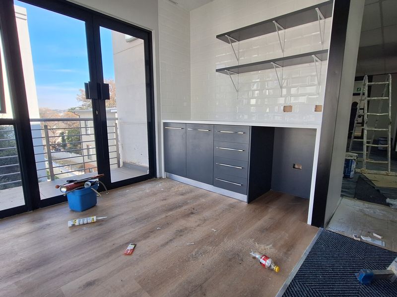 A modern kitchenette area featuring dark cabinetry, subway tile backsplash, and open shelving, with direct access to a balcony through sliding glass doors.