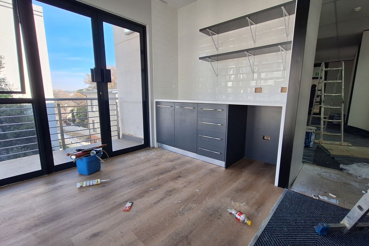 A modern kitchenette area featuring dark cabinetry, subway tile backsplash, and open shelving, with direct access to a balcony through sliding glass doors.