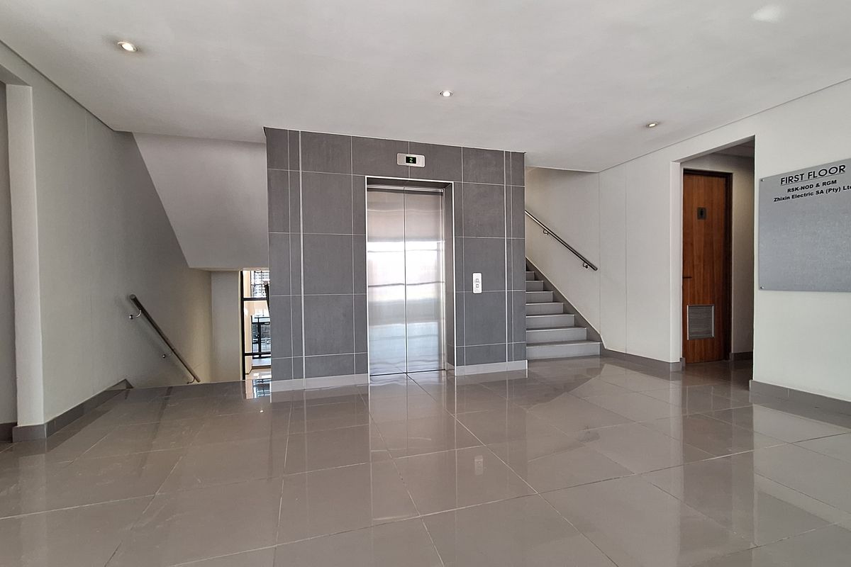 A clean and modern office building lobby featuring a central elevator, staircase access, polished tile flooring, and professional directory signage.