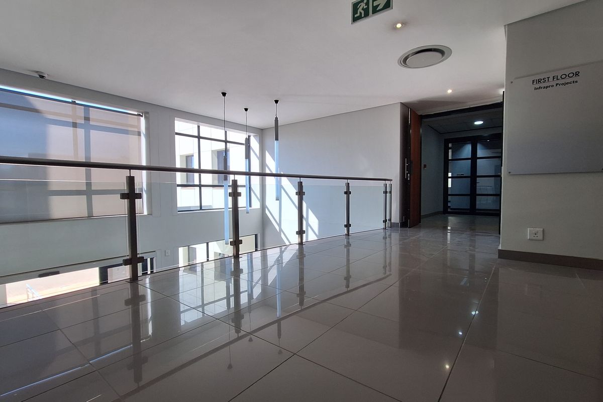 Modern office hallway featuring polished porcelain tile flooring, a sleek glass balustrade, and ample natural light from large windows.