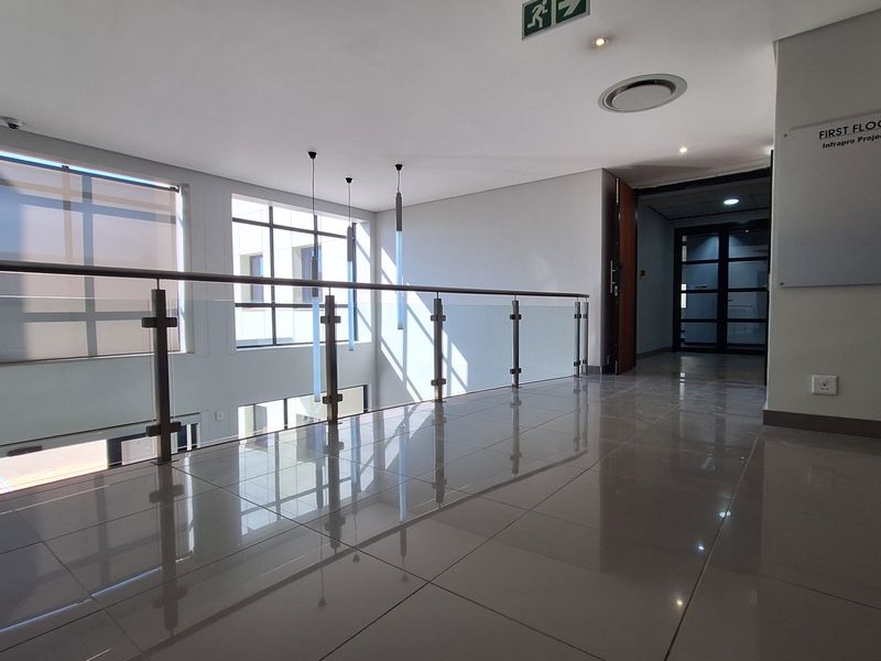 Modern office hallway featuring polished porcelain tile flooring, a sleek glass balustrade, and ample natural light from large windows.