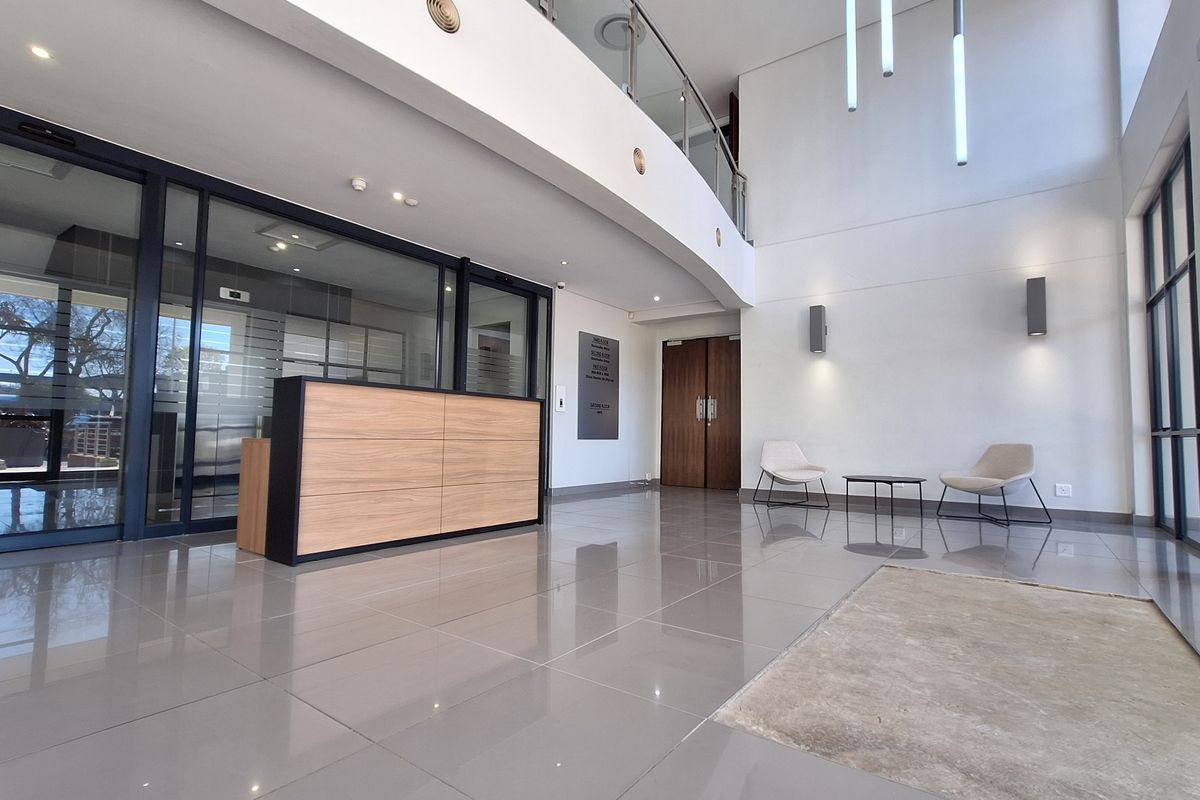 Modern double-volume office reception area featuring tiled flooring, a built-in reception desk, glass partitions, and contemporary lighting fixtures.
