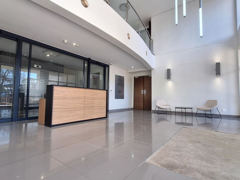 Modern double-volume office reception area featuring tiled flooring, a built-in reception desk, glass partitions, and contemporary lighting fixtures.