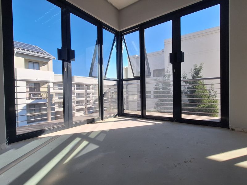 An empty, unfinished office space featuring large corner windows with balcony access, offering ample natural light and a modern architectural layout.