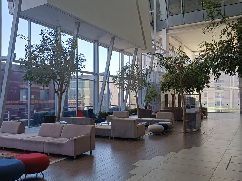 Spacious modern office atrium featuring floor-to-ceiling glass walls, high ceilings, and polished tile flooring, creating a bright and professional open-plan environment.