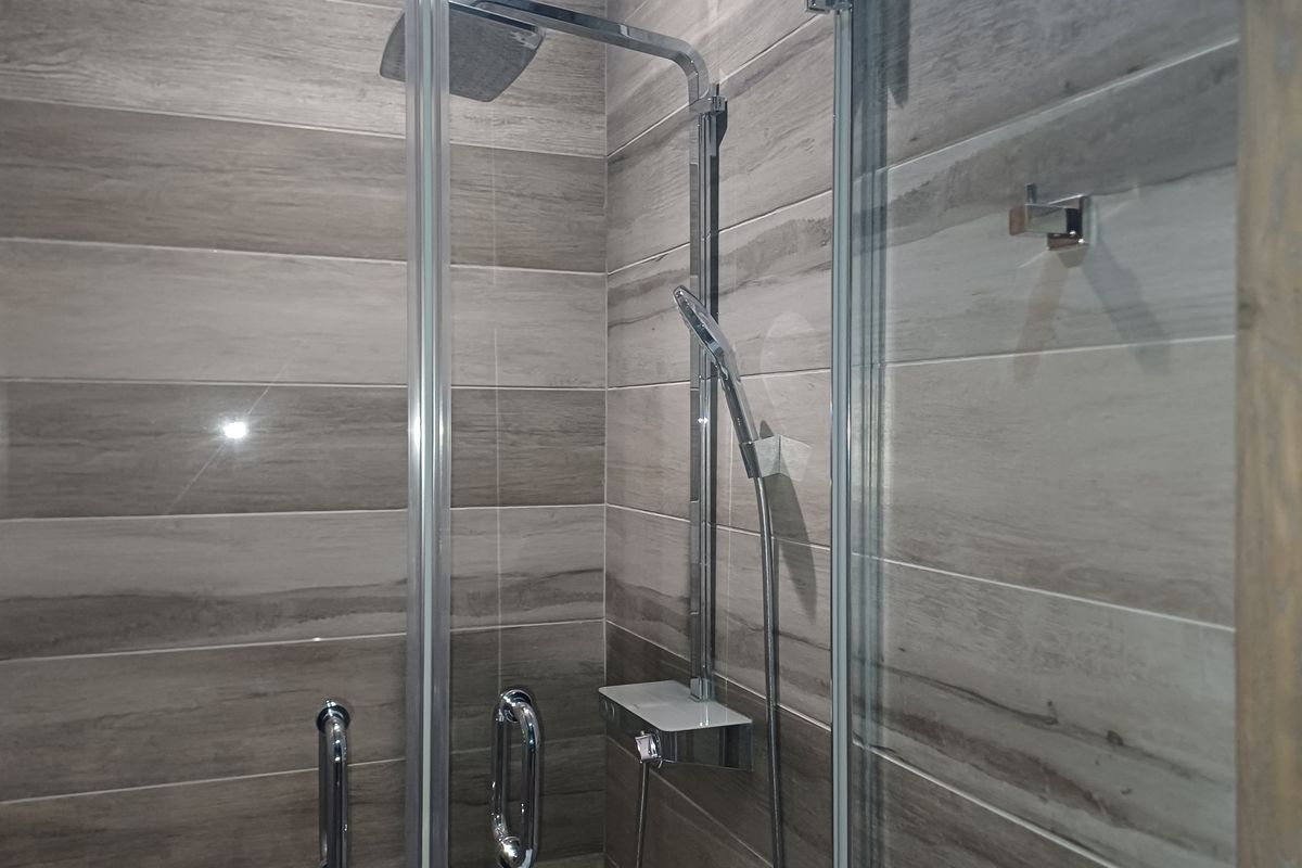 A modern, well-maintained shower stall featuring contemporary wood-look wall tiles, a glass enclosure, and high-quality chrome shower fixtures.