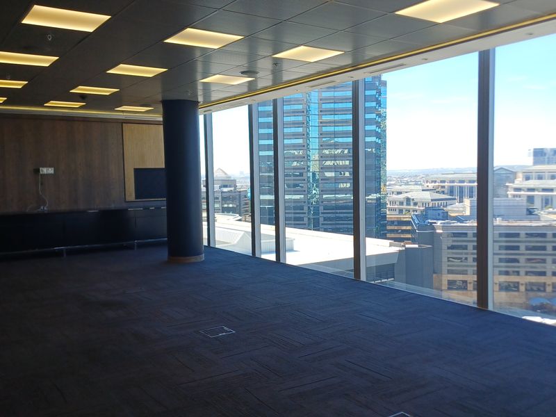 Spacious, empty office area featuring floor-to-ceiling windows with expansive city views, recessed lighting, and built-in cabinetry.