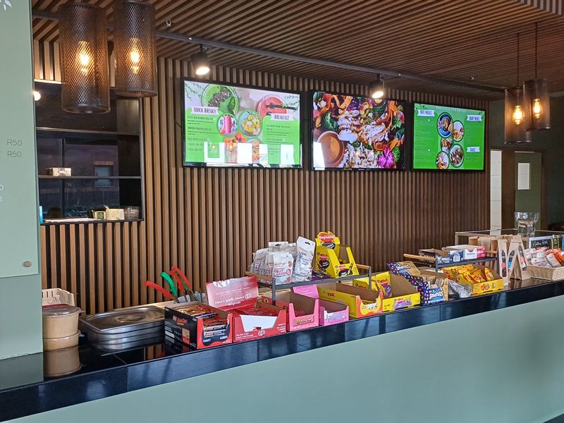 A modern commercial service counter featuring slatted timber wall and ceiling finishes, integrated digital menu boards, and contemporary pendant lighting.
