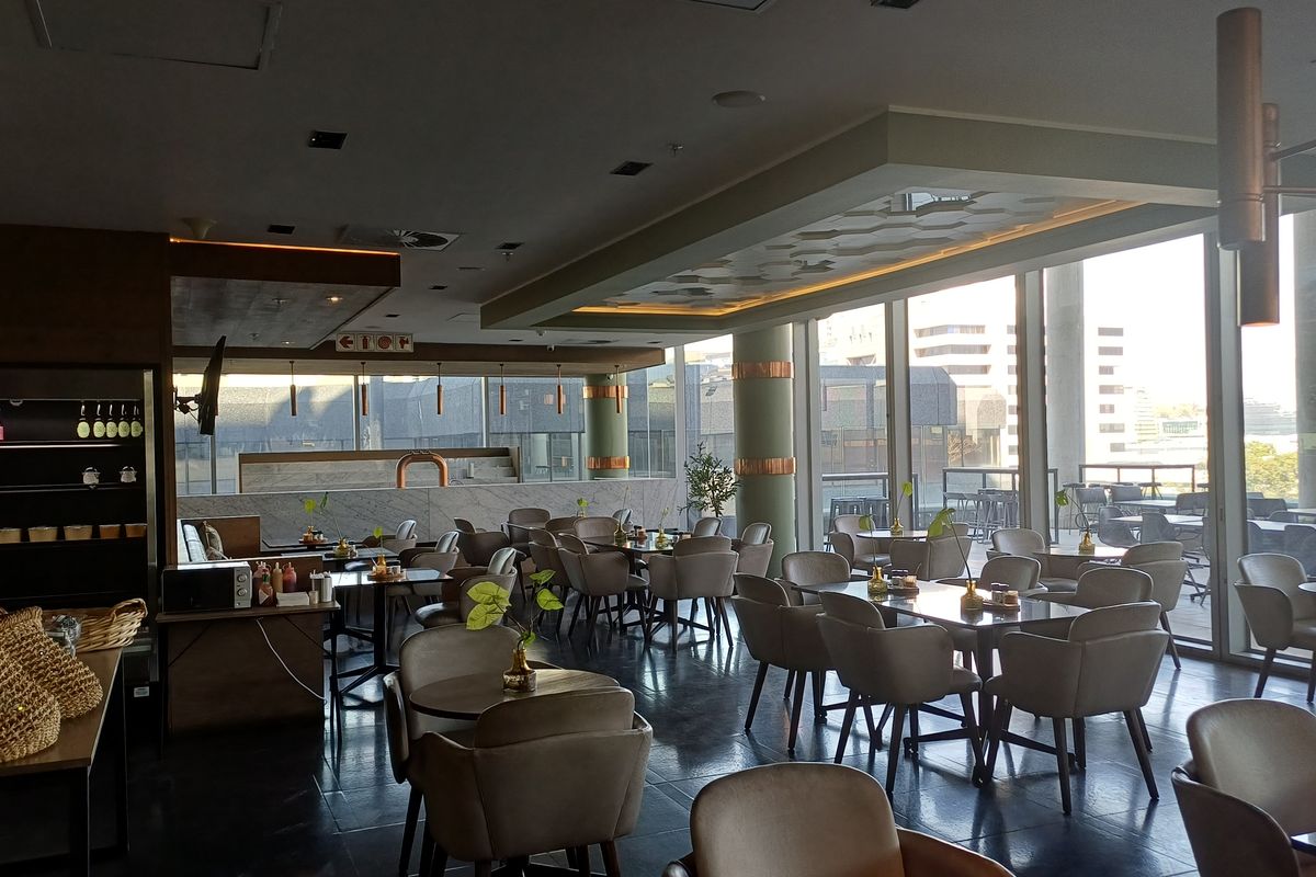 A modern, open-plan office break-out area or canteen featuring floor-to-ceiling windows, recessed lighting, and a contemporary stone-topped service counter.