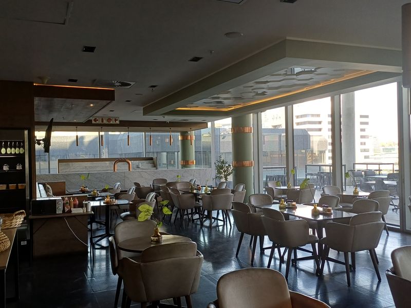 A modern, open-plan office break-out area or canteen featuring floor-to-ceiling windows, recessed lighting, and a contemporary stone-topped service counter.