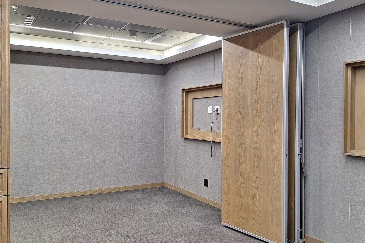 A modern, empty office space featuring acoustic wall paneling, recessed ceiling lighting, and a functional operable partition wall for flexible room configuration.