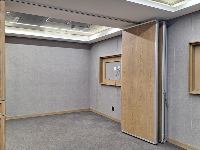 A modern, empty office space featuring acoustic wall paneling, recessed ceiling lighting, and a functional operable partition wall for flexible room configuration.