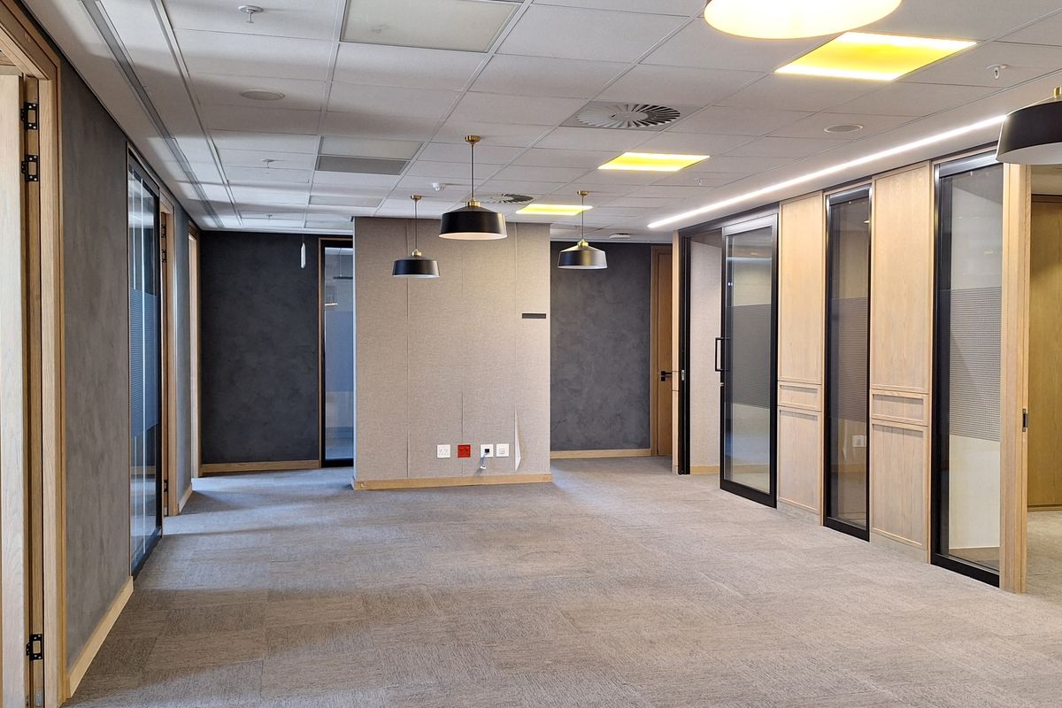 Modern open-plan office space featuring high-quality carpet tiles, suspended ceilings with integrated lighting, and sleek glass-partitioned private offices with timber accents.